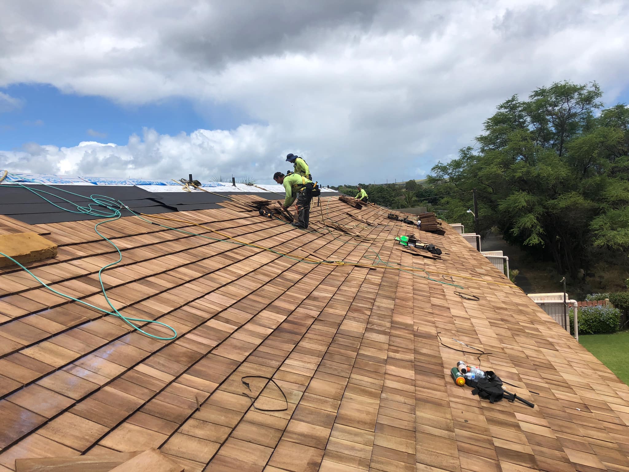 ProBuilt Hawaii crew installing cedar shake roof with safety harnesses on a large home.