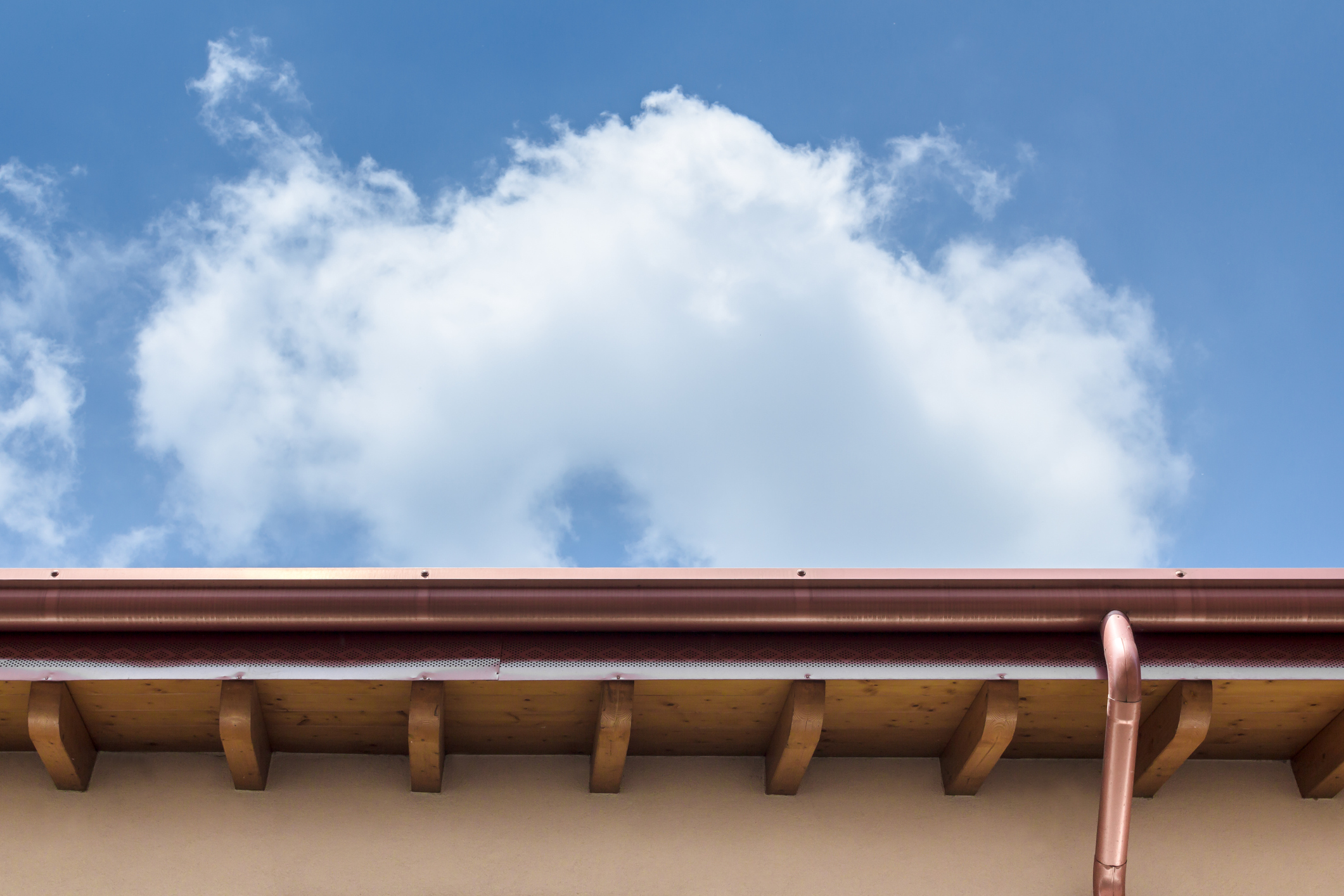 Copper gutter and downspout installed along a home in Hawaii’s roofline beneath a blue sky with clouds.